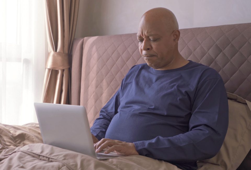 Senior Black man using a notebook laptop computer on bed in bedroom at home