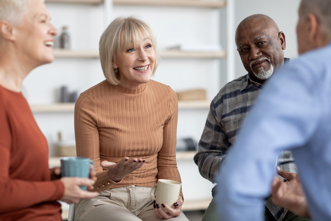 cheerful older adults sitting in circle, drinking coffee and chatting