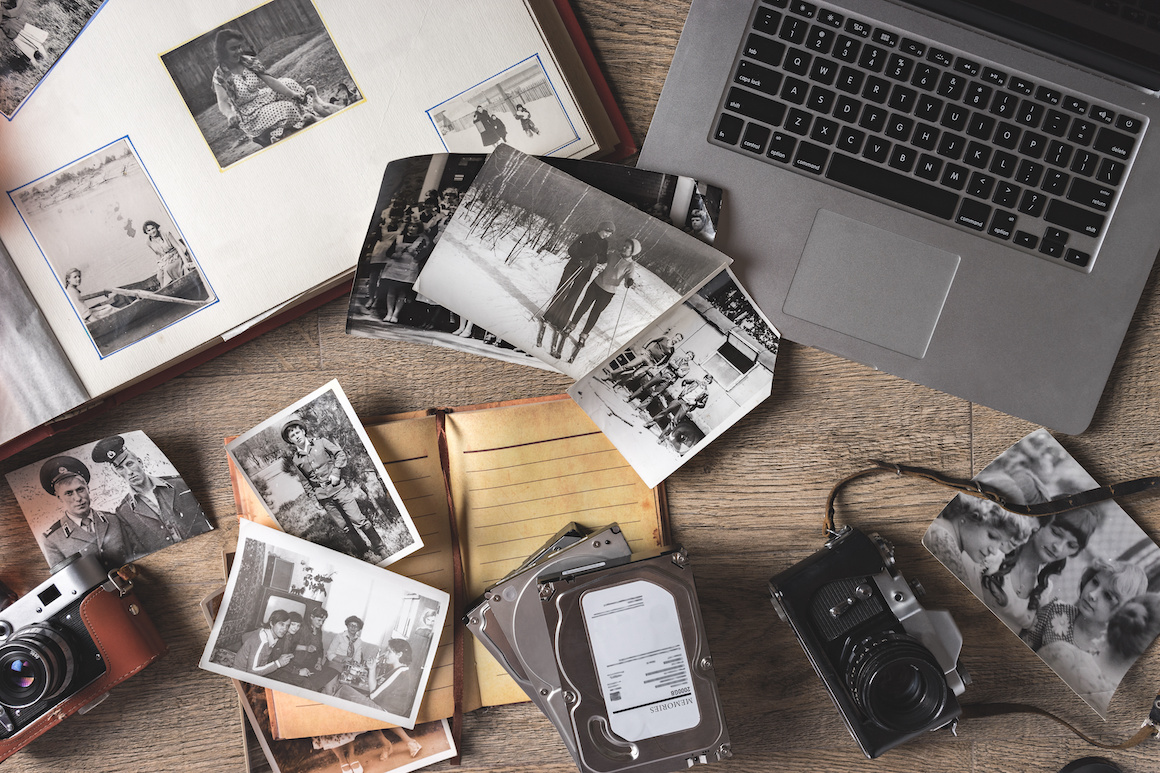 Old family photos and album on wooden background with laptop computer