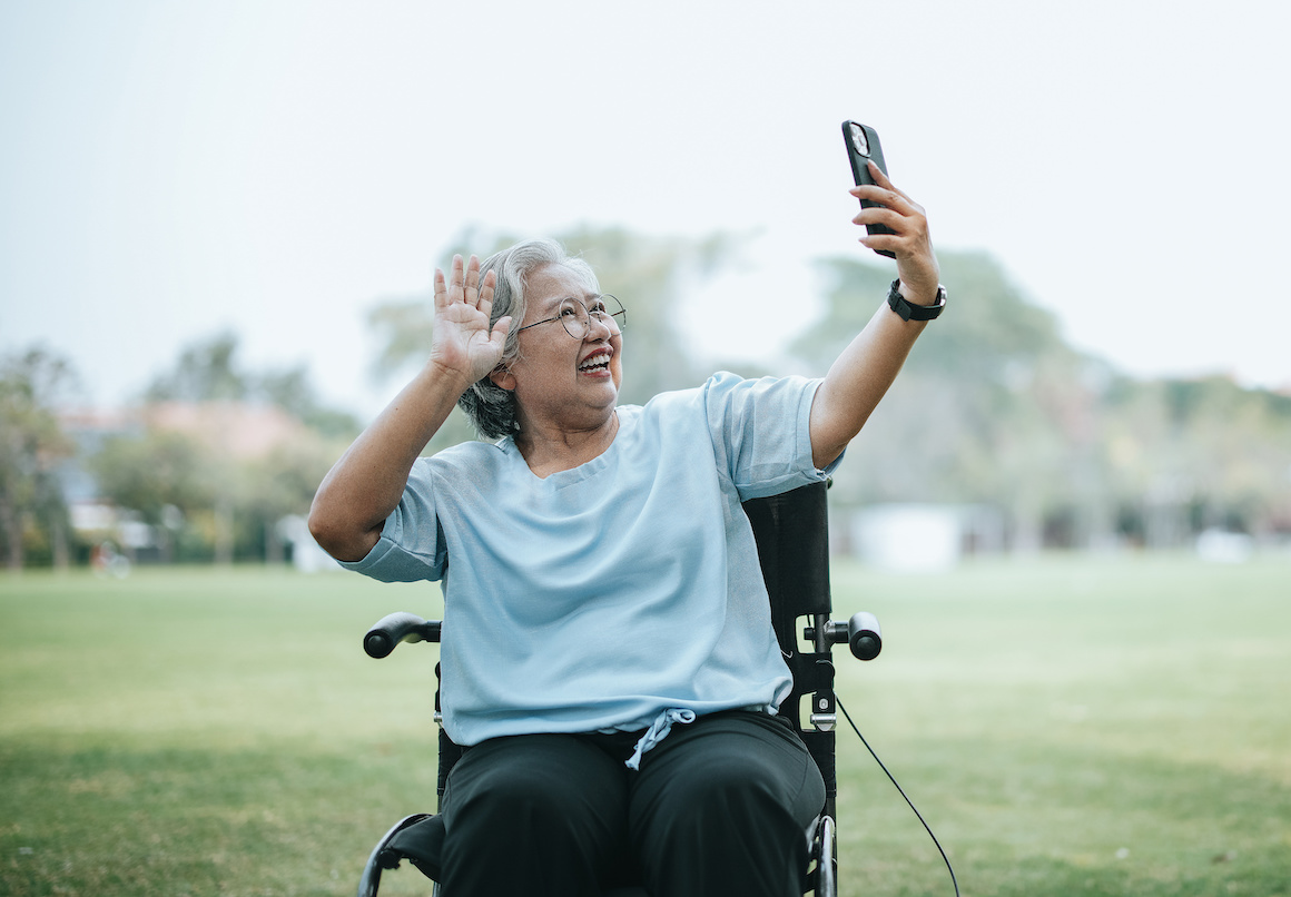 portrait of older Asian woman wearing eyeglasses sitting on wheelchair using smartphone