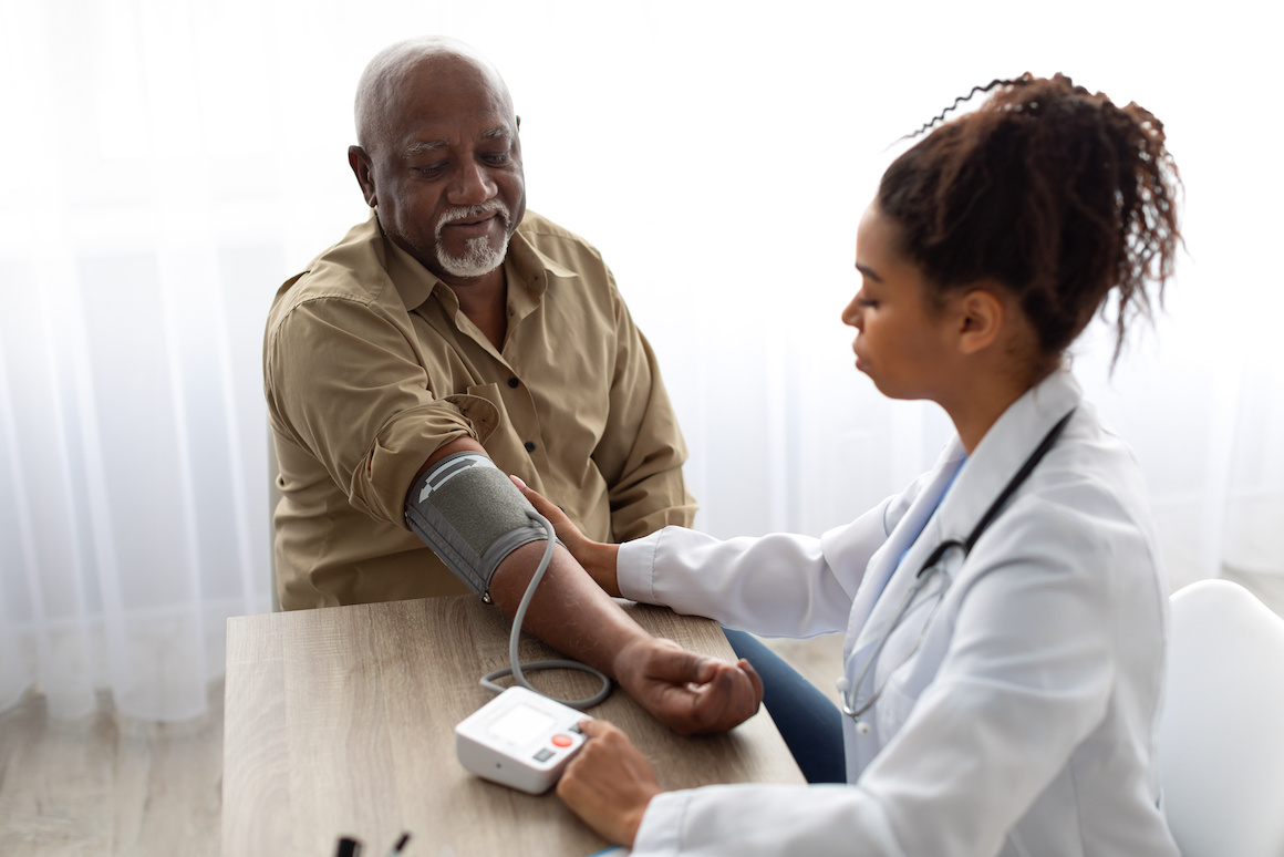 Black female doctor checking blood pressure on older adult Black male patient's arm
