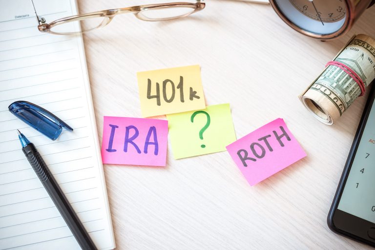 Words 401k ira roth on pieces of colorful paper, with money, dollars, and glasses on table.