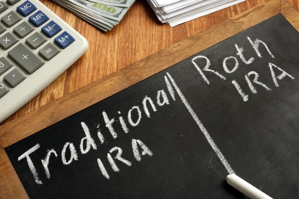 Traditional IRA vs Roth IRA written on blackboard. Calculator, money, paperwork on table.