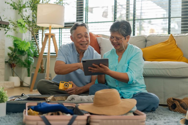 Asian retired couple using tablet online booking flight and hotel together on floor in living room at home