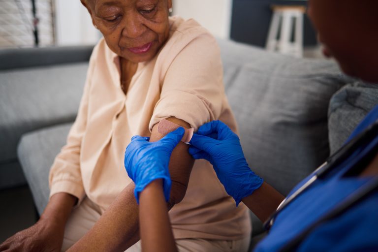 Nurse putting bandage on senior woman's arm after receiving vaccine injection.